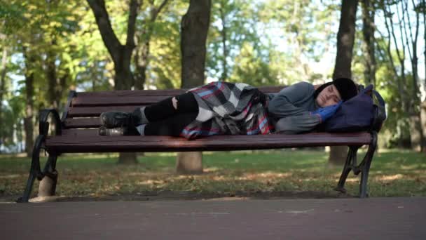 一个露宿在夏日公园长椅上的无家可归的女人被枪杀了 白种人疲惫的女流浪汉在阳光灿烂的日子里小睡片刻 无家可归和贫穷的概念 — 图库视频影像