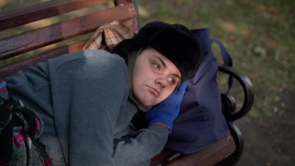 疲れホームレスの女性の肖像公園のベンチに離れて見て横たわっ 悲しい落ち込んで白人のホームレスの人は晴れた日に屋外で眠りに落ちる 不満と貧困 — ストック動画