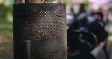 Şehir parkında arka plandaki bankta uyuyan bulanık evsiz insanların olduğu yakın çekim çöp kutusu. Kasabada çöp tenekesi ve dışarıda yatan beyaz kadın. Ağır çekim, sinema 4k ProRes karargah