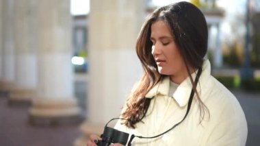 Dürbünlü, kendine güvenen genç bir kadın, kameraya bakıyor ve gülümsüyor. Açık havada poz veren güzel esmer kadın portresi.