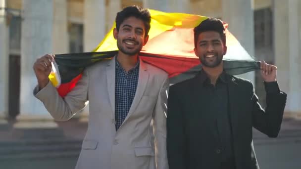 フロントビュードイツ国旗を屋外で立ってカメラを見て笑顔中東の男性 都会で晴れた日にポーズをとっている肯定的な自信に満ちた若いビジネスマン ライフスタイルと成功コンセプト — ストック動画