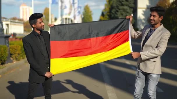 身穿西服的中东人伸展着德国国旗站在室外看着镜头笑着 两个高傲自信的小伙子举着国旗站在城市街道上 — 图库视频影像