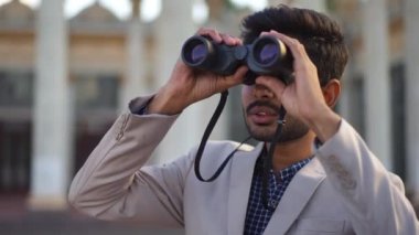 Curios Ortadoğulu genç adam şehir caddesinde duran dürbünle başka tarafa bakıyor. Zarif takım elbiseli, dışarıda gezen ve yönü seçen kendine güvenen bir adamın portresi.