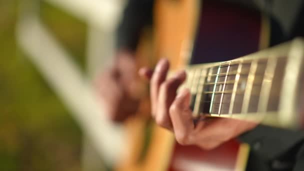 男性の手が太陽の光の下で文字列を演奏とクローズアップアコースティックギターのフロントボード 屋外の日当たりの良い公園に立って歌を演奏する認識できない若い才能中東のミュージシャン — ストック動画
