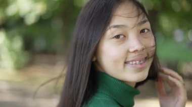 Güneşli bir yaz gününde kameraya bakıp gülümseyen neşeli kadının portresi. Sıska Asyalı genç bayanın hafta sonları dışarıda poz verip eğlendiği yakın plan çekimler. Rahatlama ve kadınlık kavramı