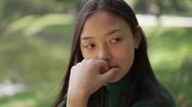 Çekici bir kadın, yüzünde gülümsemeyle Sunny Park 'ta eğleniyor. Mutlu Asyalı kadın gülerek göl kenarındaki çayırda oturuyor. Rahatlama ve yaşam tarzı kavramı