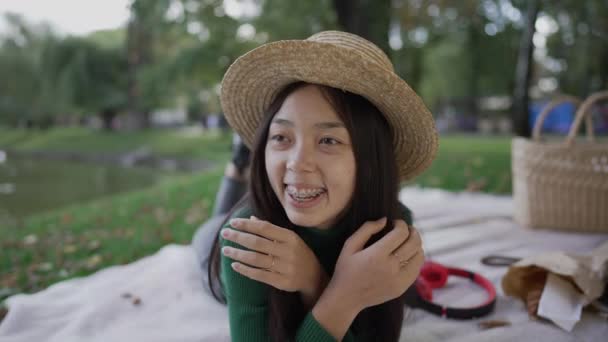 Radosna Azjatka Aparatem Zęby Uśmiechnięta Leżąca Kocu Parku Portret Zrelaksowanej — Wideo stockowe