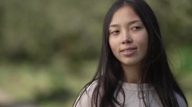 Çekici bir Asyalı kadın sağda durup kamerasını yavaş çekimde çeviriyor. Yaz parkında dinlenen mutlu güzel bayan. Yaşam tarzı ve rahatlama