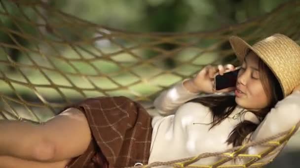 Πλευρική Άποψη Χαρούμενη Ασιάτισσα Ξαπλωμένη Στην Αιώρα Μιλώντας Στο Τηλέφωνο — Αρχείο Βίντεο
