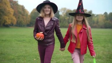 Cadı şapkalı Jack-o-Lantern 'le dışarıda el ele konuşan genç kızların portresi. Kafkas asıllı mutlu gençlerin parkta çim biçerken gülücükler atarak Cadılar Bayramı 'nın tadını çıkardığı bir resim.