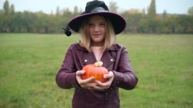Kendine güvenen pozitif gencin portresi Cadılar Bayramı kabağını esnetiyor ve dışarıda kameraya bakıyor. Beyaz kız, tatilde parkta sonbahar çayırında Jack-o-Lantern ile poz veriyor.