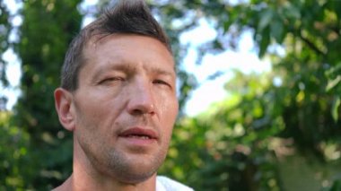 Esmer, beyaz tenli sporcunun beyaz havluyla terini silip yüzünü çeviren kameraya baktığı bir vesikalık. Yaz antrenmanından sonra arka bahçede poz veren fit, kendine güvenen bir adam.