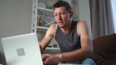 Serbest çalışanın portresi bilgisayarında baş ağrısı mesajları var. Ofiste oturuyor. Acı verici bir yüz ifadesiyle el ele tutuşan, üzgün, stresli, beyaz bir adamın orta boy fotoğrafı.