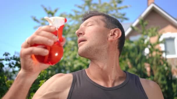 暑い夏の日に裏庭に立ってスローモーションで顔に水を噴霧白人男性 太陽の下で屋外でリフレッシュハンサムな自信家の肖像 — ストック動画