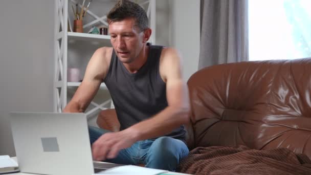ビデオゲームの瞑想で失われたラップトップ上でオンラインで吸収男のゲーム リビングルームでソファに座って大人白人男性ゲーマーの肖像画休憩 — ストック動画