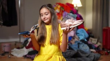 Yüksek topuklularla spor ayakkabıları arasında seçim yapıp kamera karşısında omuz silken bir genç kız. Çekici beyaz bir gencin portresi evde moda tarzı hakkında karar veriyor.