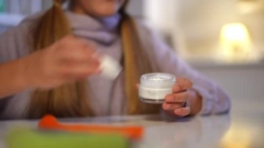 Genç kadın elleri kozmetik kavanozunu açıyor ve avuç içlerine nemlendirici sürüyor. Tanımlanamayan Kafkasyalı genç kız evde oturmuş cildine bakıyor. Güzellik rutini ve yaşam tarzı konsepti