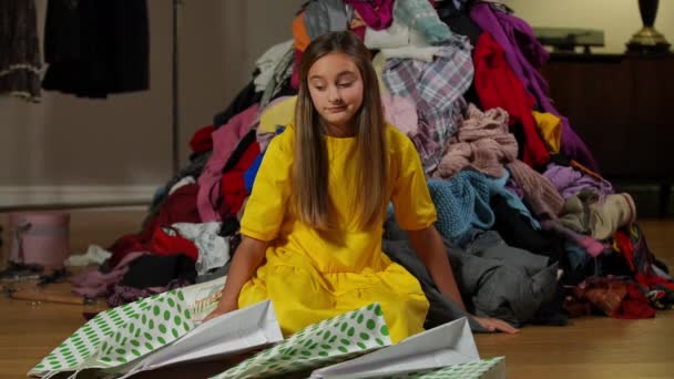 沉思的少女回头看那堆衣服 满屋子都是购物袋 具有成堆服装思维的不确定的白人青少年购物者的画像 慢动作 — 图库视频影像