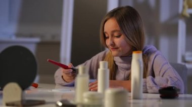 Neşeli kaygısız genç kız çene burun ve yanaklarına yüz pudrası sürerek eğleniyor. Kapalı alanda makyaj yapan beyaz bir genç ağır çekimde gülümsüyor.