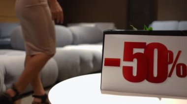Yakın plan satış duyurusu sağda bulanık beyaz kadın mobilya dükkanına giriyor arka plandaki yumuşak kanepeye oturuyor. Şablon. Kara Cuma konsepti