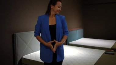 Mobilya salonundaki yüksek kaliteli yeni yatakta ortopedik yatakta oturan güzel bir kadın. Kendine güvenen beyaz zarif alıcının portresi Kara Cuma günü yeni yatak odası mobilyalarını seçiyor.