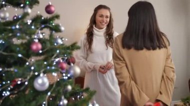 Mutlu beyaz kadın, Asyalı arkadaşına sarılıp Noel hediyesi veriyor. Mutlu genç bir bayanın portresi. Yeni yıl arifesinde evde dikilerek arkadaşını kucaklıyor.