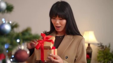 Kendine güvenen Asyalı güzel kadın içinde ışık olan hediye kutusunu açıyor ve başka tarafa bakıyor. Yeni yıl ağacının önünde Noel hediyesiyle duran mutlu ve çekici bir kadının portresi. Sürpriz konsept