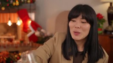 Arkadaşlarıyla kadeh tokuşturup şampanya içen gülümseyen Asyalı güzel bir kadının yakın plan portresi. Mutlu bayan evde Noel yemeğini kutluyor.