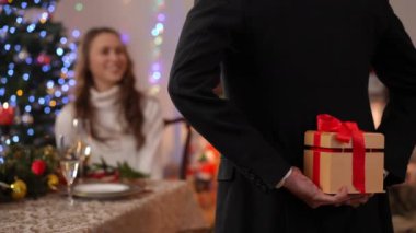 Arkadan bakıldığında, hediye kutusuyla tanınmayan zarif bir adam, arka planda oturan meraklı bir kadın, gülümseyen bir tahminde bulunuyor. Orta Doğulu koca, Kafkas karısına Noel hediyesi olarak sürpriz yapıyor.