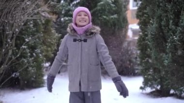Orta halli, gülümseyen, elleri esneyerek dönen genç bir kızın beyaz karın yavaş çekimde düşüşü. Heyecanlı beyaz bir gencin portresi. Bahçede kış tatilinin tadını çıkarıyor.