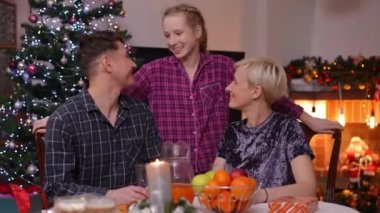 Sevimli genç kız anne ve babayla poz veriyor. Yılbaşı gecesi evde yemek masasında oturuyor. Mutlu, beyaz, kendine güveni tam bir kadın ve erkek kameraya bakıp gülümsüyor.