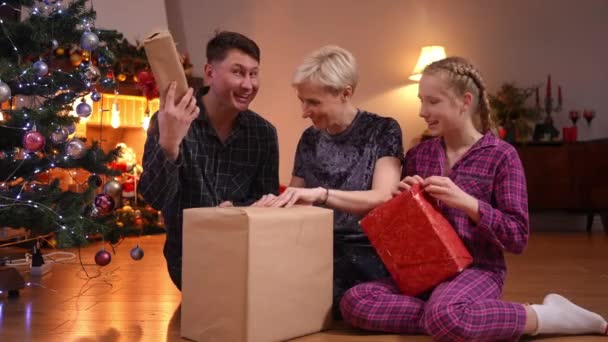 开开心心的家人坐在圣诞树前的客厅里微笑着拆开圣诞礼物 兴奋的父亲 母亲和未成年女儿一起欢度寒假的全景 — 图库视频影像