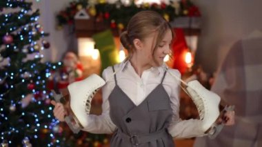 Tatmin olmuş genç bir kız yeni buz patenlerine hayran ve Noel gecesi evde durup gülümseyen kameralara bakıyor. Yeni yılda evde hediyeyle poz veren mutlu beyaz gencin portresi.