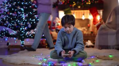 Telefon uygulamasında yeni yıl ağacını süsleyen tanınmaz kız rolünde oynayan yakışıklı beyaz bir çocuk. Kaygısız erkek kardeş, Noel gecesi için evi hazırlayan kız kardeş olarak hobisinin keyfini çıkarıyor.