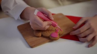 Kapalı çekimde zencefilli Noel kurabiyesi, genç bayanların el süsleme tatlısı ve pembe kraliyet kreması. Yeni yıl arifesinde evde lezzetli hamur işleri pişiren konsantre olmuş mutlu beyaz kız.