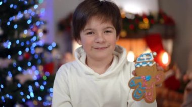 Evdeki oturma odasında zencefilli kurabiyeyle poz veren mutlu genç çocuk. Kafkasyalı gururlu bir gencin portresi kameraya bakıyor ve Noel arifesinde böbürlenerek böbürleniyor.