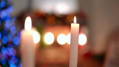 Kapalı alanda yanan beyaz mumlar ve arka planda Noel ışıkları. Yeni yıl arifesinde evde hiç insan olmadan dekorasyon yapmak. Tatil ve rahatlık kavramı