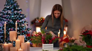 El yapımı Noel sepeti yapan gülümseyen genç bir kadının ön manzara portresi oturma odasındaki bulanık şömineye doğru yürüyor. DIY ve tatil kavramı