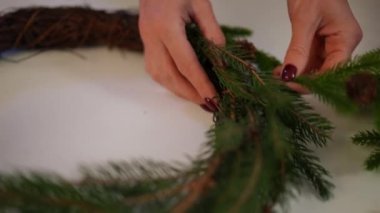 Yakın plan kadın eli, Noel çelengine çam kozalağı koyuyor. Tanımlanamayan genç beyaz kadın evinde ağır çekimde el yapımı yeni yıl süsü yapıyor.