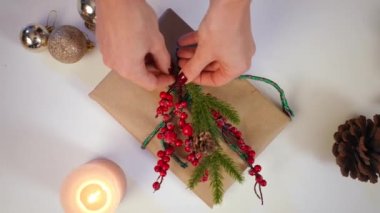 Üst düzey kadın elleri, Noel hediyesini karlı kırmızı böğürtlenlerle ve çam kozalaklı yeşil köknar dalıyla yavaş çekimde süslüyor. Tanımlanamayan Kafkasyalı genç bir kadın hediye almaya çalışıyor.