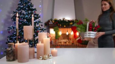 Tatmin olmuş genç bir kadın oturma odasına giriyor ve kameraya bakarak yanan mumlarla Noel sepetini masaya koyuyor. Yeni yıl arifesinde evinde poz veren kendine güvenen bin yıllık mutlu beyaz kadın.