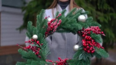 Ön manzara tanınmayan beyaz kadın ön bahçede el yapımı Noel çelengi gösteriyor. Yeni yıl dekorasyonuyla övünen sıska genç bayan. Kendin yap konseptini