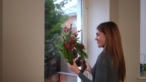 Smiling Young Woman Walking Glass Door Hanging Christmas Wreath Admiring — Stock Video