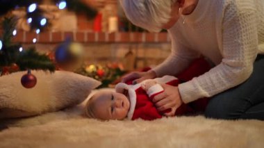 Yeni yürümeye başlayan çocukla oynayan sıska genç bir kadın olarak kameraya bakan sevimli bebek resminin yan görüntüsü. Rahatlamış Kafkasyalı kız ve anne evde Noel 'in tadını çıkarıyor.