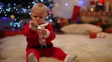 Noel süslemeleriyle oynayan sevimli küçük bir kız bebek. Kırmızı Noel Baba çantasıyla oturma odasına giren tanınmayan bir kadın olarak. Beyaz tenli çekici çocuk, annesine merakla bakıyor.
