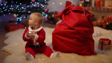 Beyaz güzel bir kızın geniş açılı portresi oturma odasında kırmızı Noel Baba çantasına oturmuş gülümseyen kameraya bakıyor. Yeni yıl arifesinde evde Noel süsüsüyle oynayan yeni yetme çocuk.