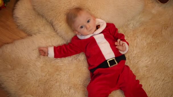 Noel Baba Kostümlü Yumuşak Halıya Uzanmış Gülümseyen Kameraya Bakan Küçük — Stok video