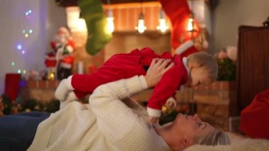 Mutlu anne oturma odasında halıya uzanmış, kızını öpüp gülümseyen bir çocuk yetiştiriyor. Beyaz tenli güzel bir bayanın Noel 'de evde bebekle oynamasına bayılıyorum.