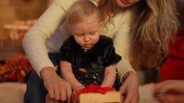 Odaklanmış güzel kız bebek Noel topuyla yavaş çekimde oynuyor. Kadın eli, içinde ışık olan hediye kutusunu açıyor. Yoğunlaşmış Kafkasyalı çocuk evde annesiyle yeni yılın tadını çıkarıyor.