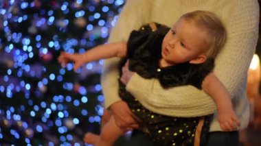 Çekici sarışın, beyaz bir kız bebek. Kadın ellerinde. İçerideki Noel ışıklarına bakarak el kol hareketi yapıyor. Yeni yıl arifesinde evde gri gözlü sevimli bir bebeğin portresi.